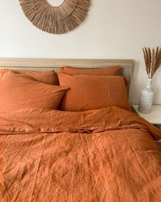 a bed with orange sheets and pillows in a bedroom next to a wall hanging on the wall