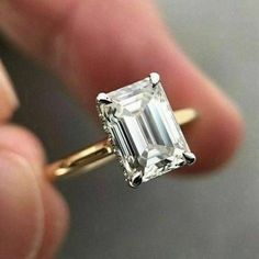 a close up of a person's hand holding a ring with an emerald stone