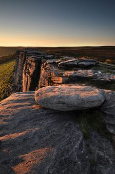 the sun is setting over some rocks on top of a hill with grass and trees in the background