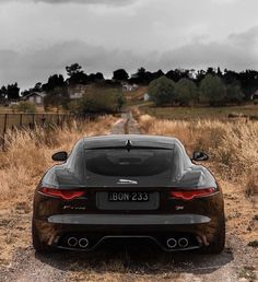 the rear end of a black sports car parked on a dirt road in a field