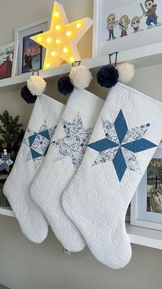 three white christmas stockings hanging from a shelf with decorations on it and a star above them