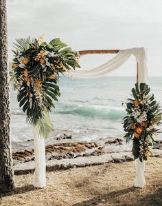 an outdoor wedding setup with white draping and tropical flowers on the arch by the ocean