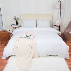 a white bed sitting on top of a hard wood floor next to a lamp and chair