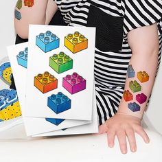 a woman with tattoos on her arm holding up some legos and building blocks stickers