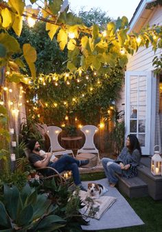 two people are sitting on the back porch with lights strung over them and a dog is laying in the chair