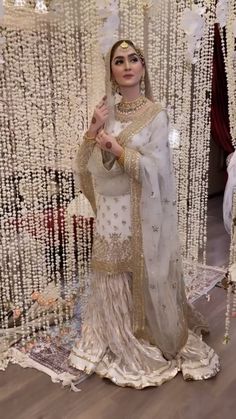 a woman in a white and gold outfit standing next to a wall with beads on it