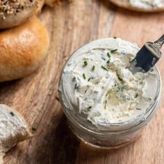 a jar filled with cream cheese sitting on top of a wooden table next to bagels