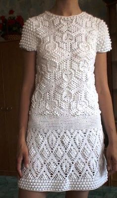 a woman standing in front of a mirror wearing a white dress with crochet on it