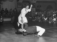 an old black and white photo of two people on a dance floor with spectators in the background