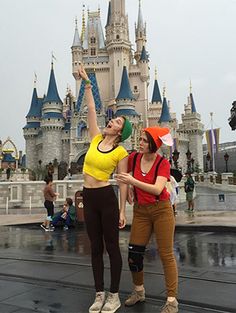 two women standing in front of a castle with their arms up to the sky and one holding an umbrella