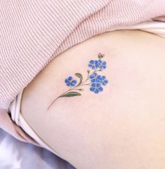 a small blue flower tattoo on the back of a woman's left side stomach