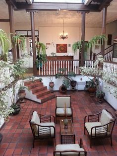 a living room filled with lots of furniture next to potted plants on top of a red tiled floor