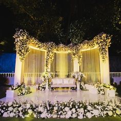 an outdoor wedding setup with white flowers and greenery on the stage, lit up at night