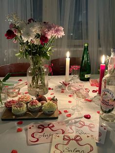 a table topped with cupcakes and flowers next to bottles of wine on top of a table