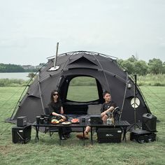 two people sitting in front of a tent with food on the table next to it