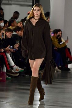 a model walks down the runway in a black shirt dress and thigh - high boots