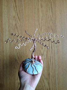 a hand holding a wire sculpture on top of a wooden table