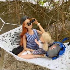 two dolls are sitting on a hammock and one is looking through the binoculars