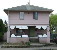 a pink house with white curtains on the front and side windows, in an urban neighborhood