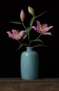 a blue vase filled with pink flowers on top of a wooden table in front of a black background