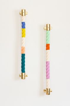 two handles made out of different colored rope and brass fittings on white wall background