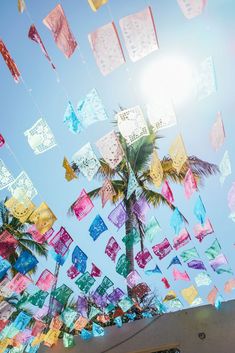 there are many colorful kites flying in the sky above some palm trees and buildings