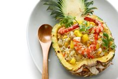 a pineapple topped with shrimp and rice on a white plate next to a wooden spoon