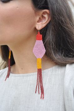 a woman wearing red, yellow and pink beaded earrings with tassels on it