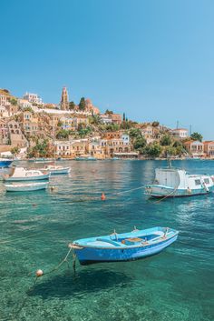 several small boats floating in the water next to a city on top of a hill