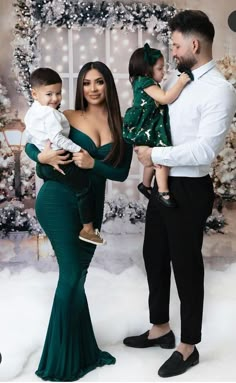 a man and woman holding a baby in front of a christmas tree