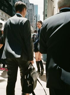 a group of people walking down a street next to tall buildings with skyscrapers in the background