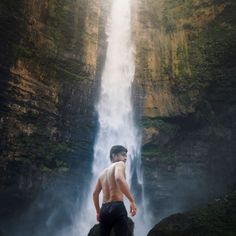 a man standing in front of a waterfall with his back turned to the camera,