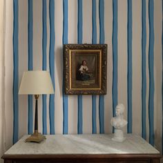 a painting is hanging on the wall next to a table with a lamp and busturine