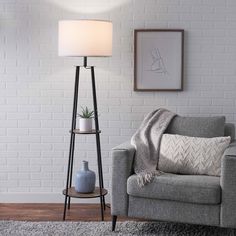 a living room with a gray couch and white brick wall behind the chair is a lamp that has a plant on it