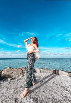 a woman standing on top of a rock next to the ocean with her arms behind her head