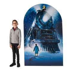 a young boy standing next to a large poster with a train on it's side