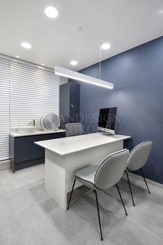 an office with two white chairs and a computer on a desk in front of a blue wall