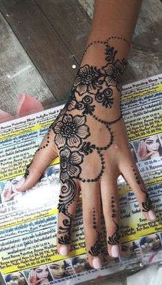 a woman's hand with henna tattoos on it and flowers around the wrist