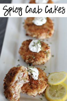 crab cakes with lemon wedges and sour cream on top are served on a white plate