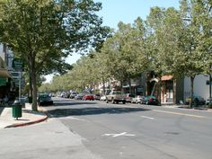 cars are parked on the street in front of buildings and trees, along with shops