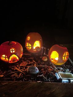 three carved pumpkins sitting on top of wood chips in the dark with glowing eyes