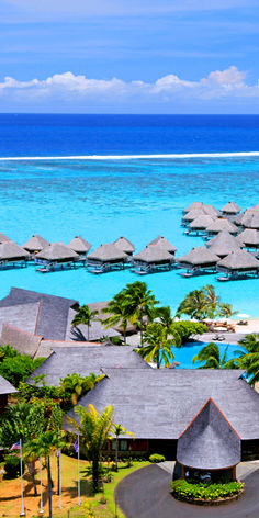 an aerial view of the ocean and resort with over water cabanas in the background