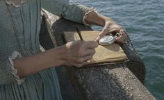 a woman is holding a pocket watch while standing on a pier near the water's edge