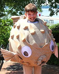 a young boy is standing in front of a giant fish costume that looks like he's smiling