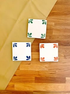 three small square dishes sitting on top of a wooden floor next to a yellow table cloth