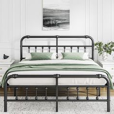 a black metal bed frame in a white bedroom with green pillows and blankets on it