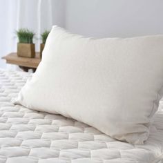 a white pillow sitting on top of a bed next to a wooden table with a potted plant