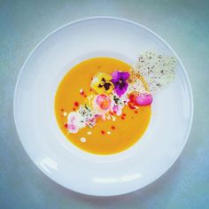 a white plate topped with an orange soup and garnished with edible flower petals