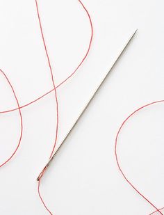 a pair of scissors sitting on top of a piece of red thread next to a needle