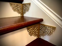 two wooden shelves on the side of a wall next to a stair case with decorative gold filigrees